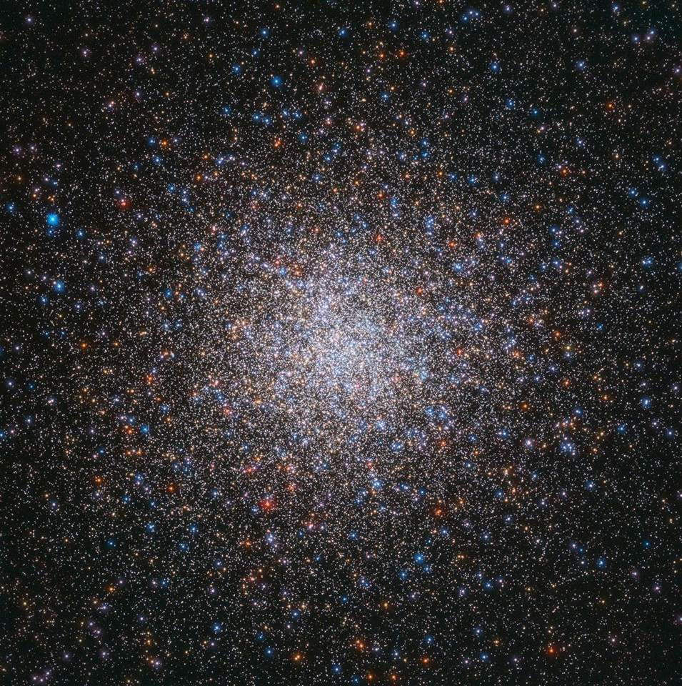 A sphere of colorful stars fills the view. Bright-white stars are concentrated at image center. Blue, red, orange and yellow stars also speckle the view.