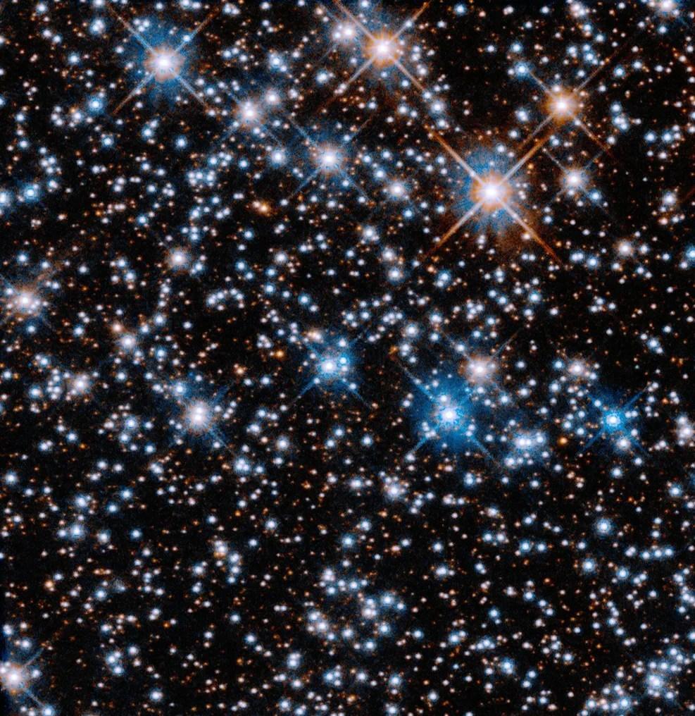 A black background is filled with small, reddish-orange stars. Larger blue-white stars are scattered across the image, with a slightly higher concentration at upper left.