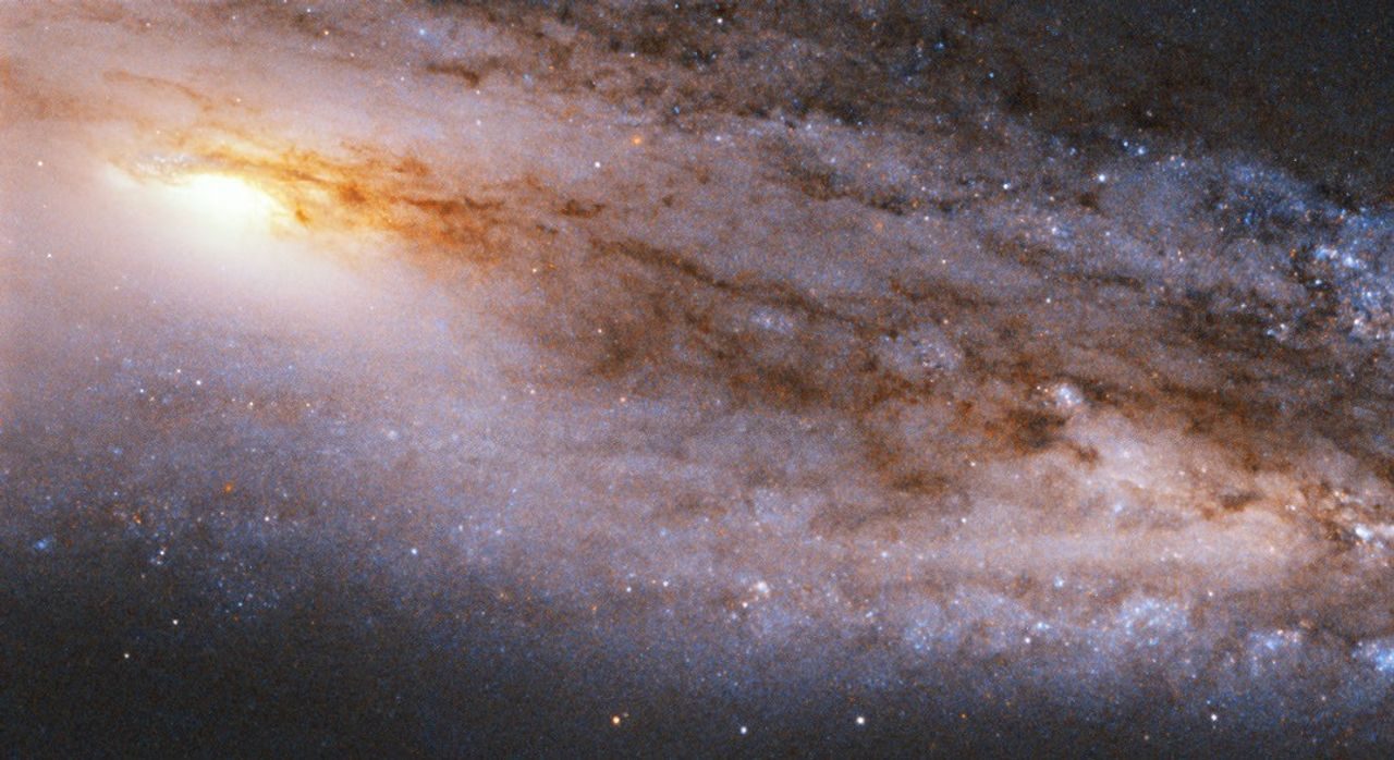 Stars, bright and dark clouds fill the view. Only a portion of the spiral galaxy is visible. Its bright core sits in the upper-left quadrant of the image.